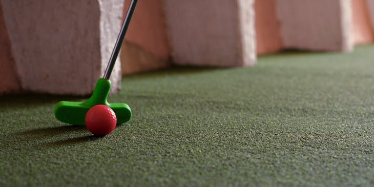 A red ball being put on a mini golf course.
