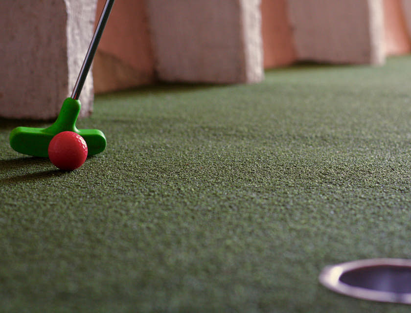 A red ball being put on a mini golf course.