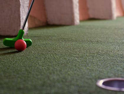 Una pallina rossa che sta per essere colpita in un campo da mini golf.
