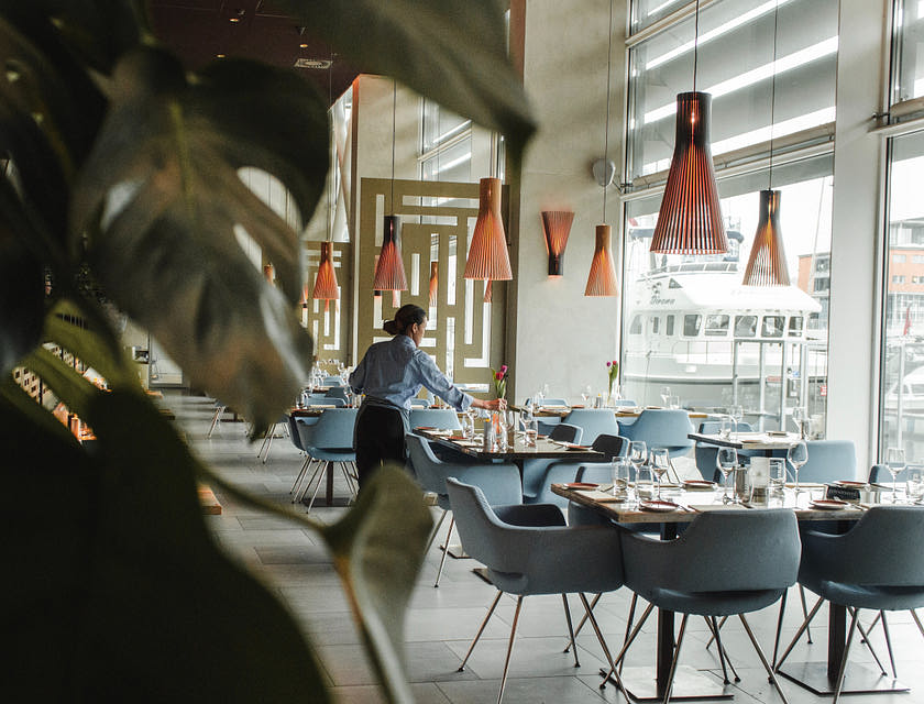 Espaço interno de um restaurante europeu com uma mulher sentada em uma das cadeiras.