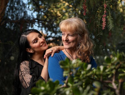 Una figlia appoggiata sulla spalla della madre in un giardino.