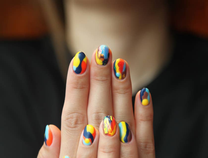 Eine Frau hält ihre manikürten Hände mit verschiedenfarbigen Fingernägeln nach einem Besuch in einem Nagelstudio hoch.