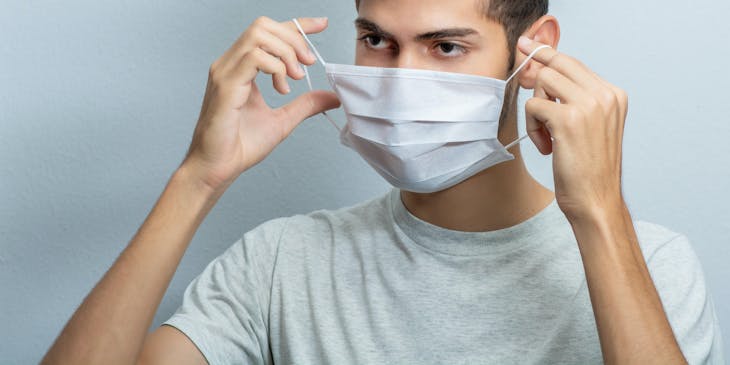 a young, casually-dressed man putting on a face mask