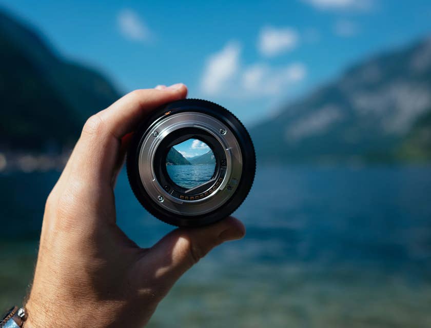Um fotógrafo de natureza segurando uma lente de câmera para a vista do lago da montanha ao fundo.
