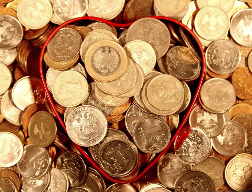 Monedas de diferentes denominaciones en un plato en forma de corazón y esparcidas sobre una mesa en un negocio abundante.