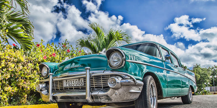 Un coche clásico azul sobre un cielo azul brillante y palmeras.