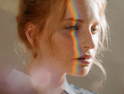 El rostro de una mujer reflejando un arcoíris en un negocio con nombre conmovedor.