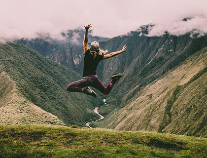 Una mujer saltando energéticamente en medio de unas montañas verdes