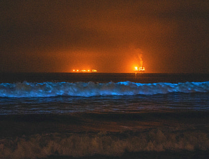 Olas del mar con brillo azul bioluminiscente en la noche con luces de barcos de agencias de tours en bahías bioluminiscentes al fondo