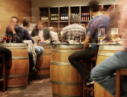 Clientes sentados alrededor de barriles como mesas, bebiendo copas de vino en un bar de chiquiteo.