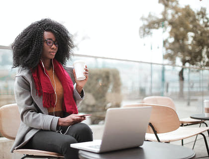 Una mujer tomando café y usando una laptop en un café Internet.