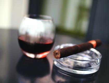 Una bebida a un lado de un cenicero con un puro en una cava de puros.