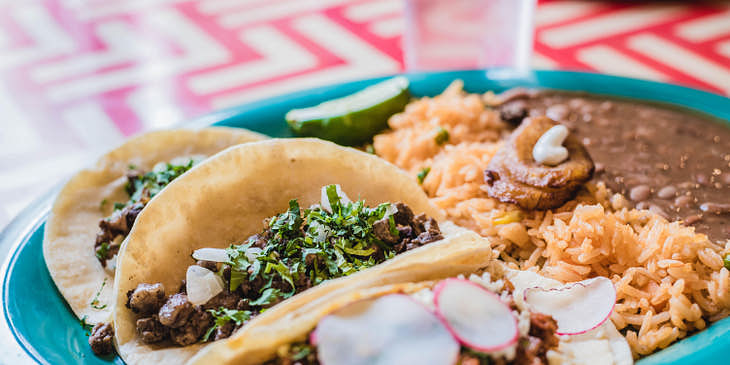 Un plato con tres tacos, frijoles refritos y arroz sobre una mesa en una cenaduría.