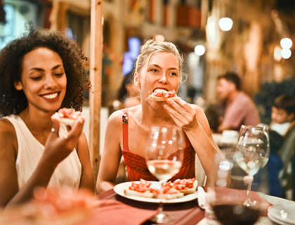 Dos mujeres tomando vino blanco y comiendo aperitivos en un centro botanero.
