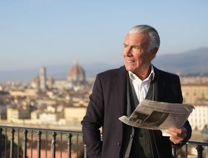Un hombre en un balcón sosteniendo un periódico de una empresa de periodismo taurino.