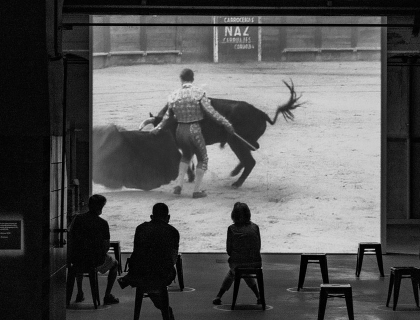 Tres personas analizando un video de un torero en el ruedo en un negocio de cursos de tauromaquia.