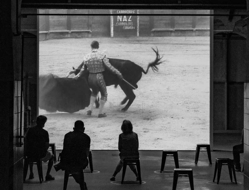 Tres personas analizando un video de un torero en el ruedo en un negocio de cursos de tauromaquia.