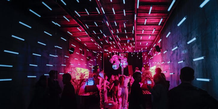 El interior de un disco bar lleno de luces neón y gente bailando y divirtiéndose.