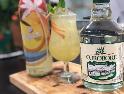 Botella de licor de cocuy sobre una tabla de madera con una copa y una botella de coctel al fondo.
