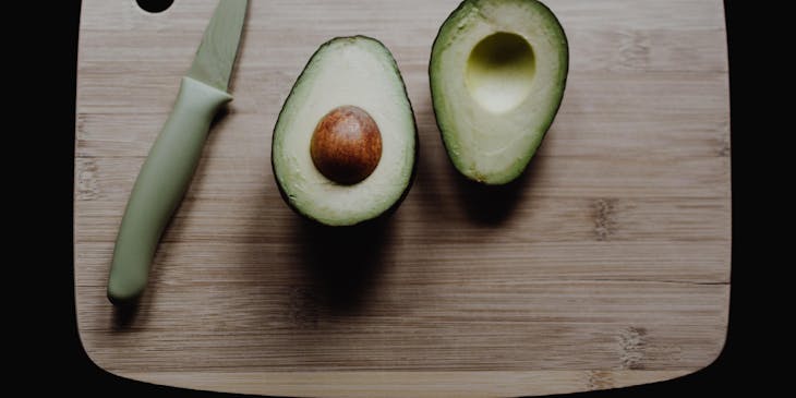 Palta peruana cortada por la mitad con un cuchillo al lado sobre una tabla de corte de madera en un fondo negro.