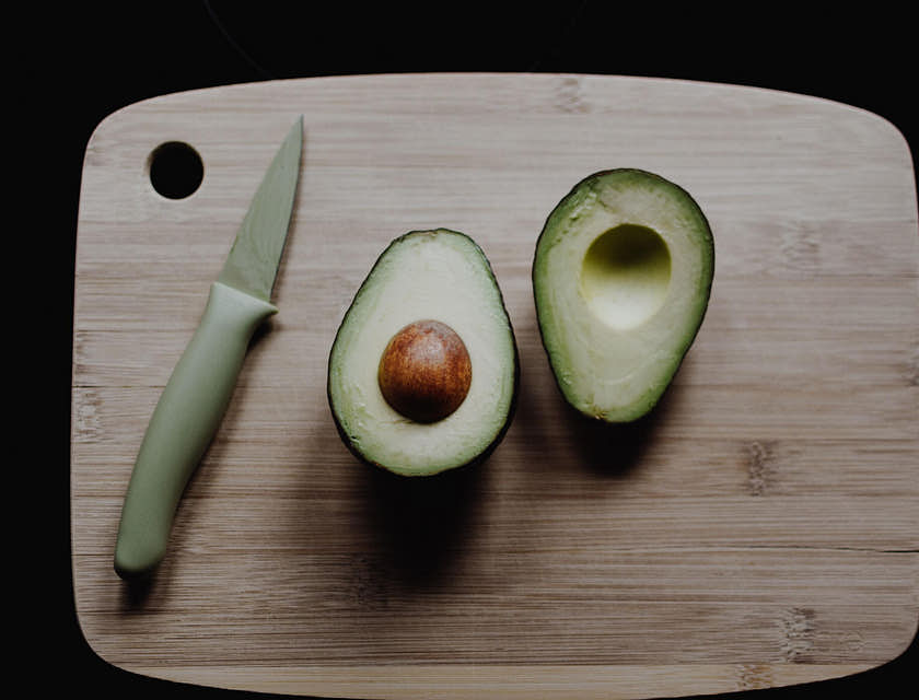 Palta peruana cortada por la mitad con un cuchillo al lado sobre una tabla de corte de madera en un fondo negro.