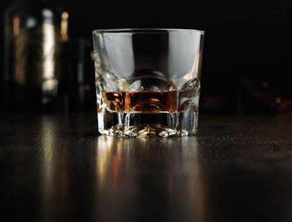 Vaso servido con ron y una botella atrás de una empresa de ron de Guatemala en una superficie y fondo oscuros.