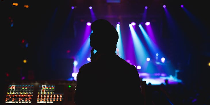 Persona operando una consola de sonido con luces de fondo en una empresa de sonido profesional.