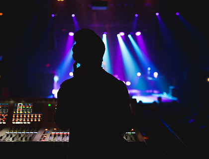 Persona operando una consola de sonido con luces de fondo en una empresa de sonido profesional.