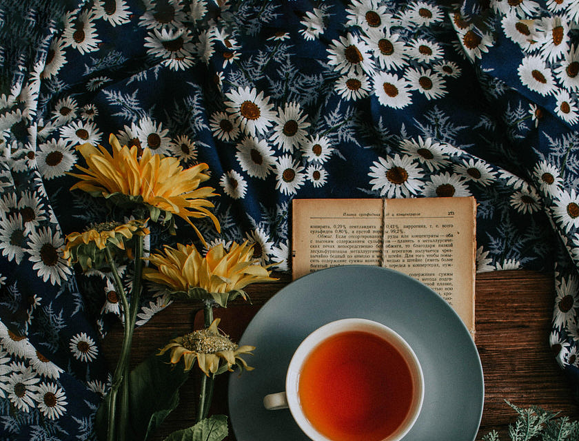 Una taza de té rojo sobre un libro y a un lado de unas flores en una empresa de té.