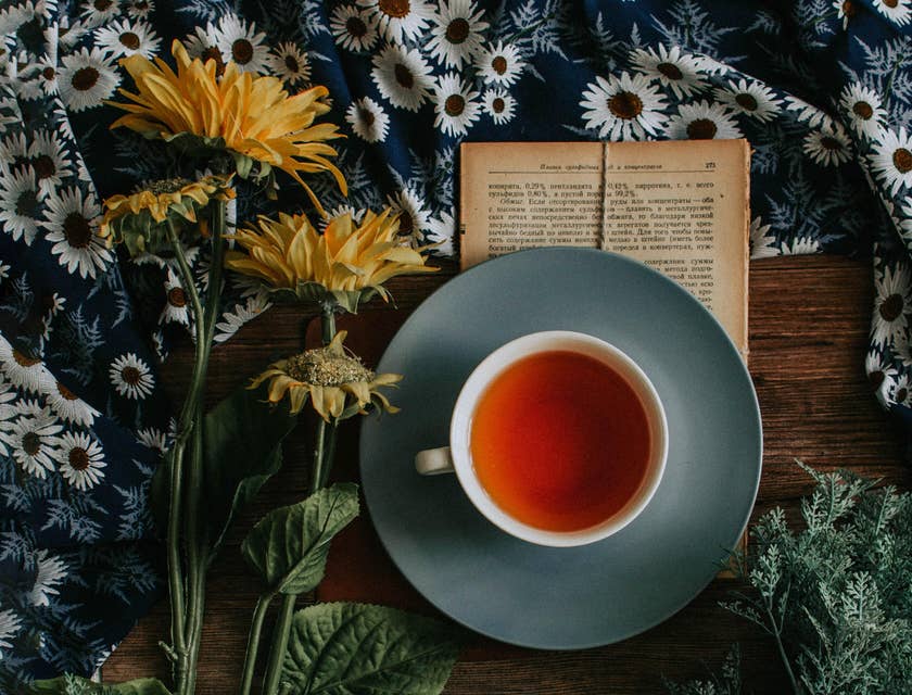 Una taza de té rojo sobre un libro y a un lado de unas flores en una empresa de té.