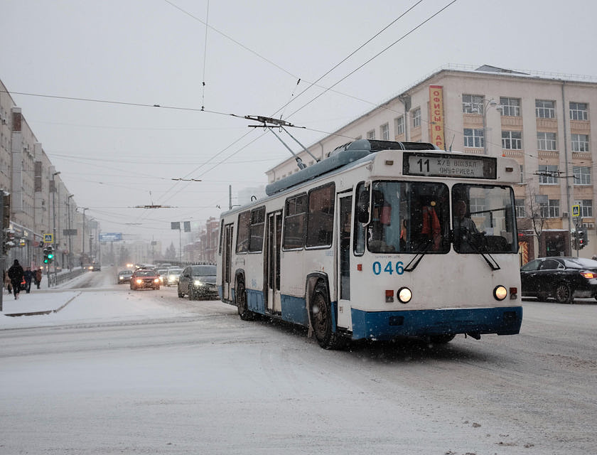 Un trolebús blanco y azul transitando por una ciudad nevada.