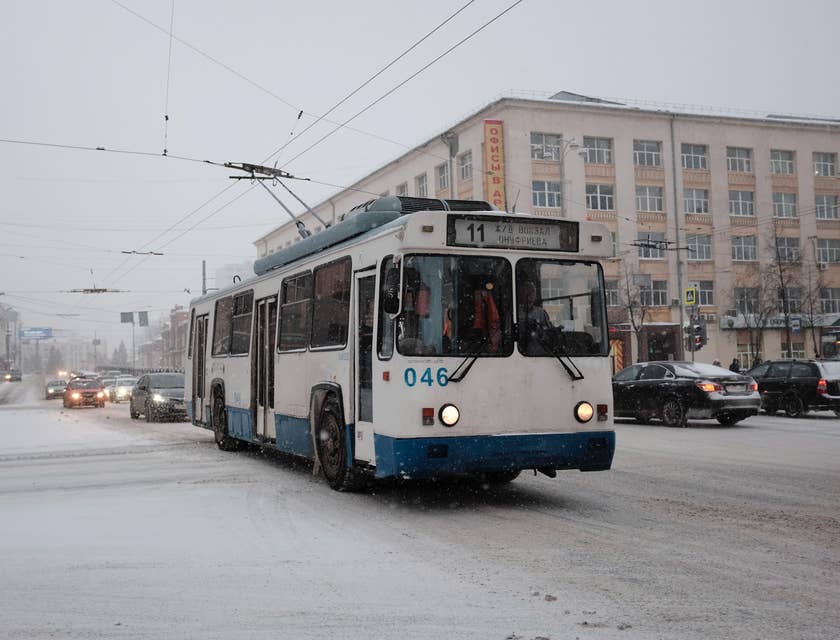 Un trolebús blanco y azul transitando por una ciudad nevada.
