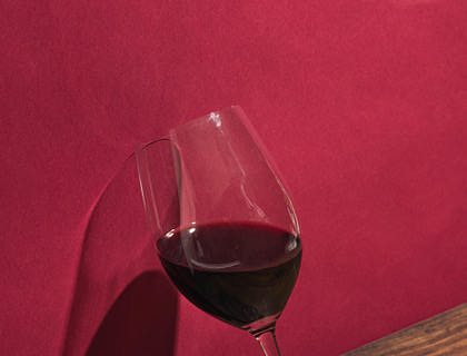 Una copa inclinada en una pared roja con vino tinto sobre una base de madera en una empresa de vinos de Mendoza.