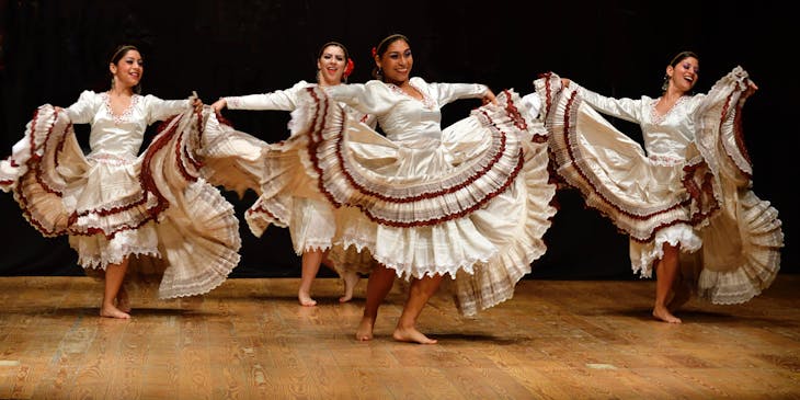 Cuatro mujeres con vestuarios típicos de su región bailando sobre un escenario en una escuela de baile joropo.