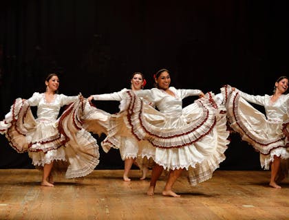 Cuatro mujeres con vestuarios típicos de su región bailando sobre un escenario en una escuela de baile joropo.