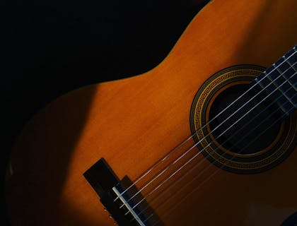 Una guitarra española entre sombras en un fondo negro en una escuela de cantaores.