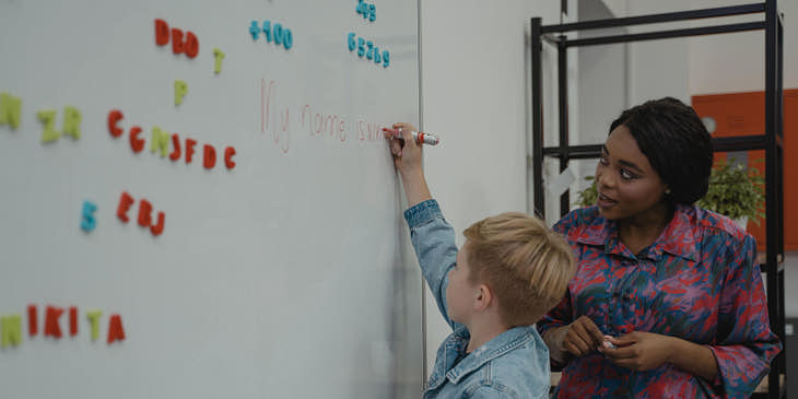 Una maestra y su alumno escribiendo en un pintarrón en una escuela de catalán.