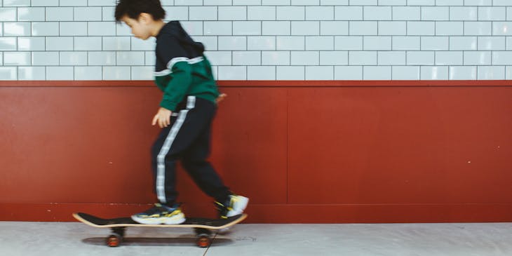 Un niño practicando en su patineta en una escuela de patinaje con fachada blanca y carmesí.