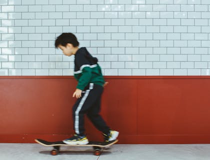 Un niño practicando en su patineta en una escuela de patinaje con fachada blanca y carmesí.