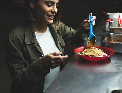 Una mujer que pone salsa a un plato con tacos en un food truck de tacos.