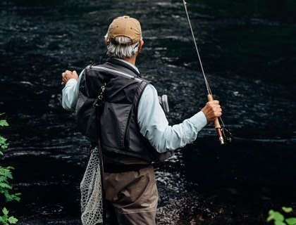 Un hombre maduro vestido con ropa adecuada para pescar y con su equipo de pesca, de parte de un grupo de pesca.