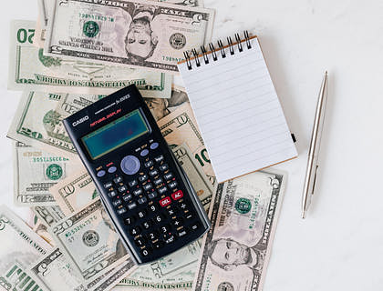 Una calculadora, una libreta, un bolígrafo y billetes esparcidos en un escritorio de un grupo de préstamos.