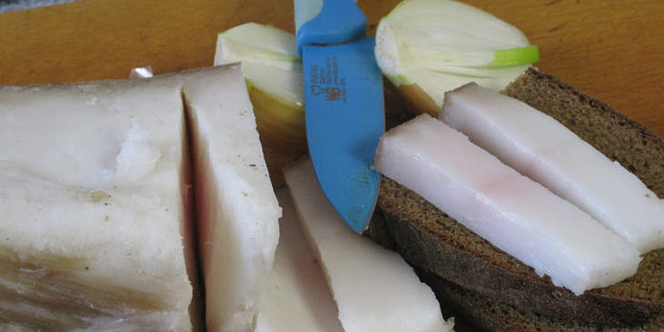 Una barra de manteca sobre una tabla de madera siendo rebanada por un cuchillo azul cielo en una mantequería.