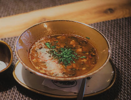 Un plato con menudo a un lado de una cuchara y un vaso pequeño con agua de horchata sobre un mantel en una mesa de una menudería.