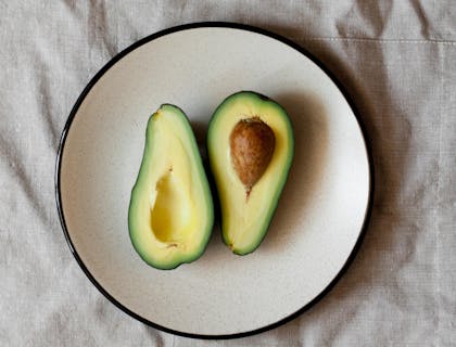 Un aguacate partido en dos sobre un plato de cerámica blanco sobre un mantel blanco en una mesa de un negocio de aguacate.