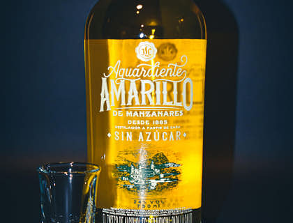 Botella de aguardiente con un vasito a la izquierda en fondo azul en un negocio de aguardiente.