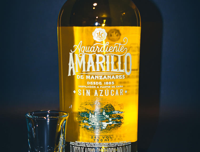 Botella de aguardiente con un vasito a la izquierda en fondo azul en un negocio de aguardiente.