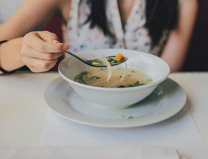 una mujer tomando una cucharada de ajiaco en un plato hondo en un negocio de ajiaco