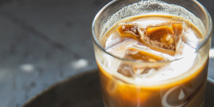 Una vaso lleno de bebida junto a un postre servidos en una mesa de un negocio de aloja