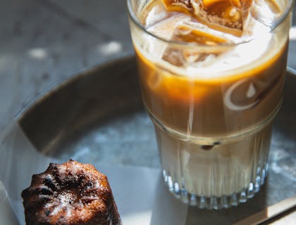 Una vaso lleno de bebida junto a un postre servidos en una mesa de un negocio de aloja